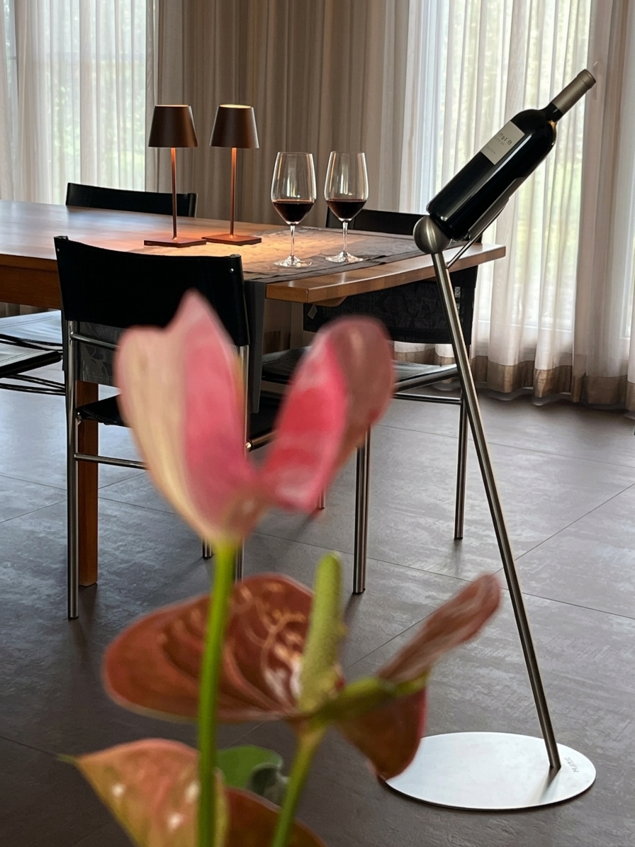 NOAH Weinständer aus Chromstahl mit Weinflasche im warm beleuchteten Esszimmer, im Vordergrund eine Blüte